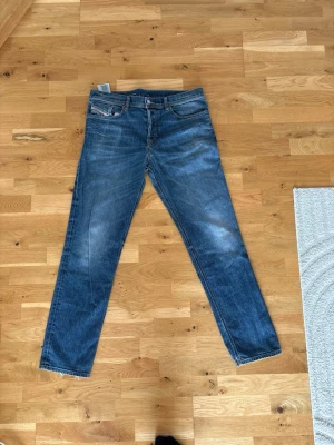 Blåa straight fit jeans från Levi's - Säljer ett par klassiska blåa jeans från diesel  med straight fit och fem fickor. Jeansen har slitningar och ljusare partier på låren för en cool vintage-look. Materialet är denim och modellen har råa kanter vid benslut. Perfekt för dig som gillar tidlös stil.
