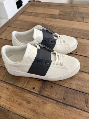 Valentino Garavani vita sneakers - Snygga vita sneakers från Valentino Garavani med mörkblå rem över snörningen och logga på plösen. Skorna är i nyskick, endast använda någon gång bara.      