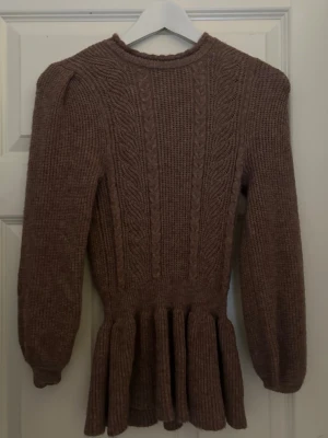 Brun peplumstickad tröja från ONLY - Supersnygg brun stickad tröja från ONLY med peplumdetalj i midjan och kabelstickat mönster framtill. Tröjan har långa ärmar, rund halsringning och ribbade muddar. Ny pris 250kr