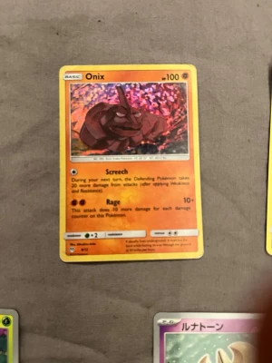 Onix Pokémonkort holografiskt - Säljer ett holografiskt Onix Pokémonkort med färgstark bakgrund och tydliga illustrationer. Kortet har gula kanter och text på engelska. Perfekt för samlare eller Pokémonfans som vill utöka sin kortsamling.