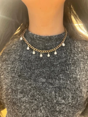 Guldfärgat halsband med pärlor - Snyggt halsband i guldfärgad metall med kedja och hängande vita pärlor. Kedjan har en chunky stil och pärlorna är droppformade, vilket ger en trendig och elegant look. Perfekt accessoar för att lyfta din outfit.