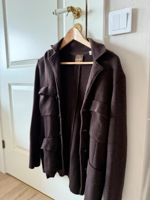 Brun cardiganjacka med fickor - Mörkbrun cardiganjacka från Stenströms med fyra stora fickor framtill och knäppning med knappar. Jackan har klassisk krage och är tillverkad i ett mjukt, stickat material som ger en avslappnad men stilren look. Nypris ca 4000