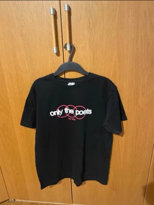 Only The Poets svart tour t-shirt - Tröjan är använd 2-3 gånger men i den är i nyskick. Svart t-shirt från Only The Poets med tryck fram och bak från 'holding onto memories tour 2025'. Framsidan har vit och rosa text, baksidan listar turnéstopp. Klassisk passform och rund hals. Perfekt för dig som gillar bandmerch och streetwear.