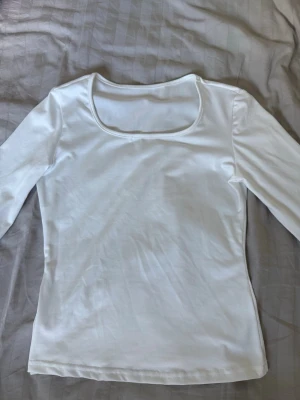 Vit långärmad topp - En enkel och stilren vit långärmad topp med rundad halsringning. Tillverkad i ett mjukt och stretchigt material som sitter bekvämt på kroppen. Perfekt att matcha med jeans eller kjol för en clean look. Helt oanvänd