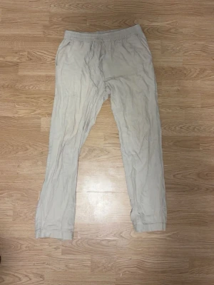 Beiga mjukisbyxor med resårmidja - Säljer ett par beiga mjukisbyxor med resår i midjan och raka ben. Byxorna har sidofickor och är tillverkade i ett mjukt, tunt material som passar perfekt för chill dagar. Enkla att matcha med hoodie eller t-shirt.