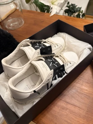 Valentino Garavani vita sneakers - Säljer mina vita sneakers från Valentino Garavani med svart detalj och stor stjärna på sidan då de inte längre kommer till användning. Skorna har vita snören, svart panel med logga och är tillverkade i läder. F
