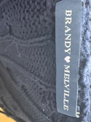 Marin blå zip up hoodie från Brandy Melville  - Mysig mörkblå zip up hoodie med dragkedja framtill och huva. Tröjan har ett diskret kabelstickat mönster. Perfekt för dig som gillar en avslappnad och stilren look. 