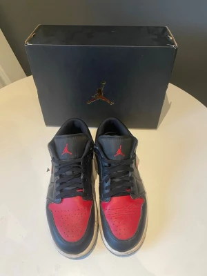 Air Jordan 1 low - Säljer nu mina low Jordan 1 blivit för små för mig, lite smutsiga på underskon men det är inget som man behöver bry sig om. Vänstra skon är lite creasad. Röda detaljer och svart runt om.