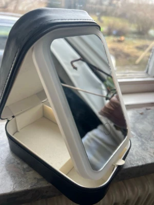 Sminkspegel med förvaringsbox - Snygg sminkspegel med vit ram och praktisk förvaringsbox i svart konstläder. Spegeln är rektangulär och locket kan ställas upp för enkel användning och med ledd lampa runt och USBC uttag till spegeln . Perfekt att ha på sminkbordet eller ta med på resan för att hålla ordning på dina sminkprylar.