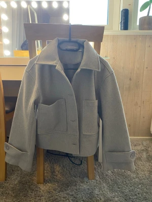 Grå kappa - Säljer en grå oversized jacka i ullmix med stora fickor framtill och bred krage. Jackan har stora knappar och breda ärmslut med knappdetalj. Perfekt för dig som gillar minimalistisk och trendig stil. Pris kan diskuteras 