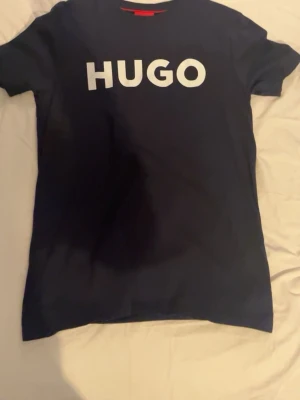 Två trendiga t-shirts från Hugo & Hoodrich 2 för400 - Säljer två snygga t-shirts! En svart Hugo t-shirt med stor vit logga framtill och en vit Hoodrich t-shirt med coolt tryck på ryggen. Båda har klassisk passform och är kortärmade, perfekta till jeans eller shorts.