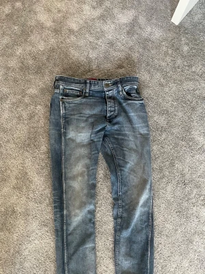 Blå slim fit jeans från Jack & Jones - Snygga blå slim fit jeans från Jack & Jones med klassisk femficksdesign och slitningar på benen. Jeansen har en cool tvättad look och är tillverkade i denim med kontrastsömmar. Perfekta för dig som vill ha en modern och avslappnad stil.