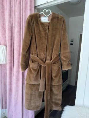 Tiger of Sweden kappa i fuskpäls – modell Solferino – storlek  NY / S - Tiger of Sweden kappa i fuskpäls – modell Solferino – storlek  NY  Elegant och mjuk kappa från Tiger of Sweden i brun fuskpäls. Rak, stilren modell med bälte i midjan och fickor. Mycket varm och lyxig känsla. Perfekt både till vardag och mer uppklätt.  • Märke: Tiger of Sweden • Modell: Solferino • Storlek: S • Färg: brun / camel • Material: fuskpäls • Med bälte och fickor • Skick: oanvänd / mycket fint skick  Nypris ca 4300–5000 kr Pris: 1200 kr (kan diskuteras)  Kan skickas eller hämtas.