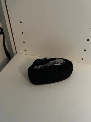 Svart flätat bälte i syntet - Snyggt svart flätat bälte i syntetmaterial. Perfekt för att ge din outfit en stilren touch. Bältet har ett klassiskt spänne i metall och passar till både jeans och byxor.