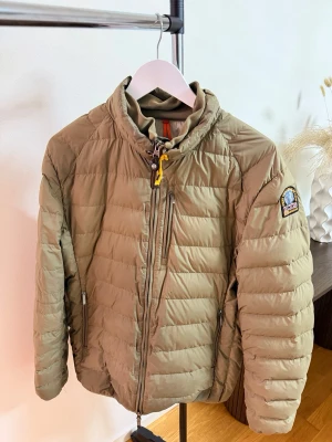  Parajumpers - Snygg olivgrön dunjacka från Parajumpers med quiltad design, hög krage och dragkedja framtill. Jackan har tre fickor med dragkedja och den klassiska Parajumpers-loggan på ärmen. Perfekt för kalla vinterdagar storlek XL