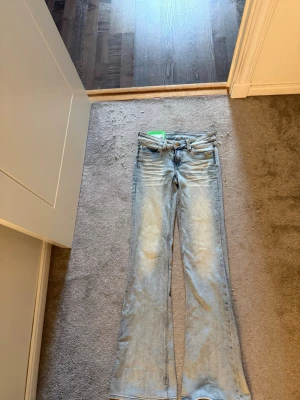 Ljusblå bootcut jeans  - Säljer ett par ljusblå bootcut jeans med utsvängda ben och låg midja. Jeansen har en grön broderad detalj på bakfickan och klassisk femficksdesign. Perfekta för en avslappnad och trendig look. Materialet är denim i bomull. Nytt skick då jag aldrig använt dom och därför jag säljer dom, lappen är även kvar. Pris kan diskuteras!