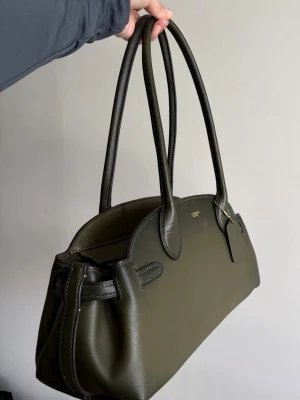 Olivgrön handväska från Coach (Empire Carryall 34) - Olivgrön handväska från Coach. Väskan har dubbla långa handtag och diskret logga framtill. Den är endast använd ett fåtal gånger, är i felfritt skick.