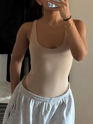 Beige basic body med djup rygg - Säljer en stilren beige body med breda axelband och djup urringning både fram och bak. Bodyn har en tight passform och är tillverkad i ett mjukt, stretchigt material som sitter skönt mot kroppen. Perfekt att styla under jeans eller kjol för en clean look.