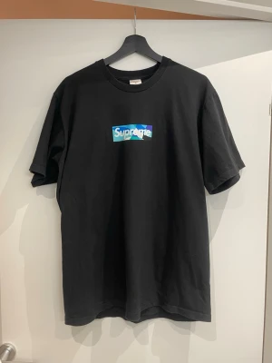 Supreme x Emilio Pucci Box Logo Tee Black/Blue – Size M - Säljer en Supreme x Emilio Pucci Box Logo Tee i svart/blå – en av de mer unika box logo-releaserna från Supreme.  Detta är en collab med Emilio Pucci, vilket gör den betydligt mer speciell än vanliga box logo tees. Den har det ikoniska Pucci-mönstret i box logon och är eftertraktad bland Supreme-samlare.  ✔ 100% äkta ✔ Storlek M ✔ Väldigt bra skick (använd fåtal gånger) ✔ Inga fläckar eller hål ✔ Trycket i fint skick  Perfekt för dig som vill ha en clean hype piece eller bygger en Supreme-collec
