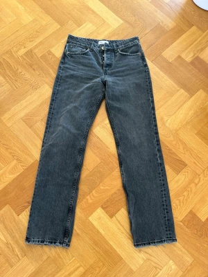 Svarta raka jeans mid waist - Snygga svarta jeans med rak passform och rå, fransad kant nedtill. Klassisk femficksmodell och knappgylf. Jeansen har en tvättad look och är tillverkade i denim. Perfekta för en avslappnad och trendig stil.