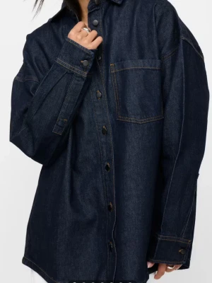 Mörkblå oversized jeansjacka - Stilren mörkblå jeansjacka i oversized modell med klassisk krage, knappstängning och en bröstficka. Jackan har kontrastsömmar och långa ärmar med manschetter. Perfekt för en avslappnad och trendig look. Om du har några frågor, är det bara att fråga dem! 😊