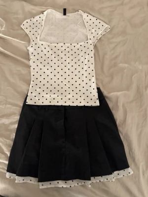 Svart kortkjol med prickig kant - Säljer en svart kortkjol med bred linning . Kjolen har en vit underkjol med svarta prickar som sticker fram längst ner och ger en söt kontrast. Perfekt för dig som gillar en lekfull och trendig stil ( storlek xs). Och tröjan är prickig i storlek xs, den är perfekt med olika byxor eller Tjol!.