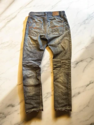 Nudie Jeans sharp bengt - Snygga blå slim fit jeans från Nudie Jeans med klassisk femficksdesign och slitningar på både fram- och baksida. Jeansen har en tvättad look med ljusare partier och kontrastsömmar. Tillverkade i bomull med en skön passform och läderpatch bak i midjan.