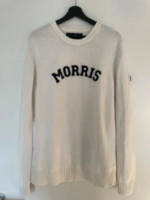 Morris stickad tröja – vit – L - Klassisk stickad tröja från Morris i stilren vit färg. Tidlös modell med broderad Morris-logga framtill och patch på ärmen. Perfekt till både vardag och mer uppklädda outfits.  ✔ Storlek: L ✔ Färg: Vit ✔ Material: 100% bomull ✔ Skick: Bra skick