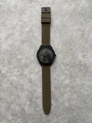 Hysteric Glamour klocka - Stilren klocka med olivgrönt silikonband och svart rund boett. Urtavlan har en modern design med synliga detaljer och röda visare som sticker ut. Perfekt accessoar för dig som gillar en clean och sportig look. 🚨Battery needs to be replaced🚨