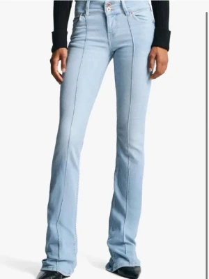 Ljusblå bootcut jeans med pressveck - Säljer ett par ljusblå bootcut jeans med markerade pressveck framtill. Jeansen har hög midja, klassiska fem fickor och stängs med knapp och dragkedja. Tillverkade i stretchig denim för skön passform. Perfekta för en avslappnad men trendig look.