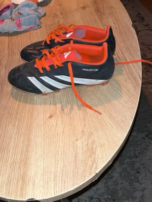 Adidas Predator svart/vit fotbollssko - Säljer ett par klassiska Adidas Predator fotbollsskor i svart med vita detaljer och orange snörning samt innersula. Skorna har låg profil och är designade för bra grepp på planen. Perfekta för dig som vill ha kontroll och stil på fotbollsplanen.