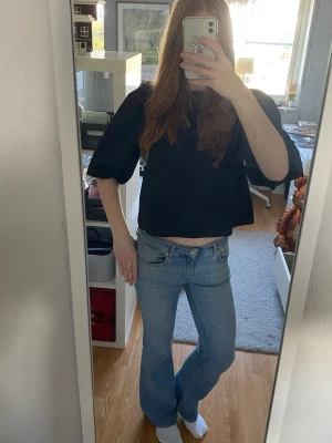 Svart croppad topp med rosetter - Trendig svart croppad topp med puffiga ärmar och öppen rygg som knyts med två stora vita rosetter. Perfekt för dig som vill ha en unik och söt detalj på din outfit. Toppen har en loose passform och är riktigt snygg till festliga tillfällen. Bara använt en gång 💕