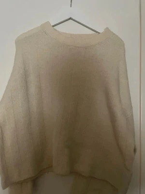 Beige oversized stickad tröja - Mysig beige stickad tröja med bred passform och diskreta vertikala ränder. Tröjan har rund halsringning och långa ärmar. Perfekt för lager på lager och chill dagar. Materialet känns mjukt och skönt mot huden.