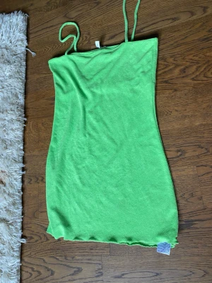 Grön ärmlös kortklänning - Snygg grön kortklänning med smala axelband och enkel, rak passform. Klänningen är ärmlös och har en mjuk, något stretchig textur som ger en bekväm känsla. Perfekt för varma dagar och enkel att styla med accessoarer.