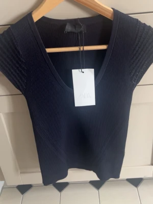Mörkblå ribbad topp från Zara - Snygg mörkblå ribbad topp från Zara med v-ringning och korta ärmar. Toppen har en figurnära passform och är tillverkad i ett stretchigt material som ger en bekväm känsla. skriv för fler bilder!