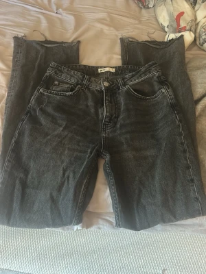 Svarta raka jeans med rå kant - Säljer ett par svarta raka jeans med råa, avklippta benslut. Klassisk femficksmodell med hög midja och dragkedja. Jeansen har en tvättad look och är gjorda i kraftigt denimtyg. Perfekta för en avslappnad och trendig stil.