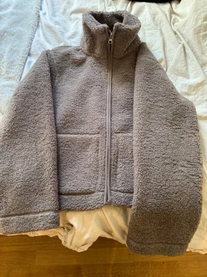 Brun teddyjacka från 157 - Mysig brun teddyjacka från 157 i storlek XS. Jackan har hög krage, dragkedja framtill och två stora fickor. Tillverkad i fluffigt teddy-material som håller dig varm och ger en chill look.