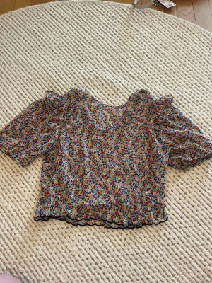 Blommig blus med puffärm - Söt blommig blus med kort puffärm och vågig kant nertill. Tunt och luftigt material, perfekt för varma dagar. Färgglatt blommönster i rött, blått, grönt och gult. TVEKA INTE OM FRÅGOR!🌸🌼🌺