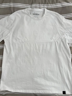 Vit relaxed fit t-shirt Pull&Bear - Klassisk vit t-shirt från Pull&Bear i relaxed fit. Tillverkad i mjuk bomull med rund halsringning och korta ärmar. Enkel och stilren design utan tryck eller mönster, perfekt till alla outfits.