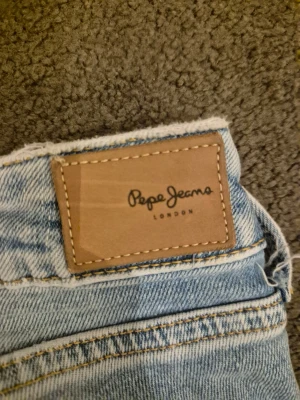 Ljusblå raka jeans från Pepe Jeans - Säljer ett par ljusblå jeans från Pepe Jeans med klassisk femficksmodell och raka ben. Jeansen har en snygg tvättad look och detaljerade sömmar. Perfekta för en avslappnad och trendig stil. Materialet är denim i bomull. De är mid till lowwaist (sitter mitt på höftbenet) och är av modellen piccadilly från Pepe jeans. Mycket bra skick!