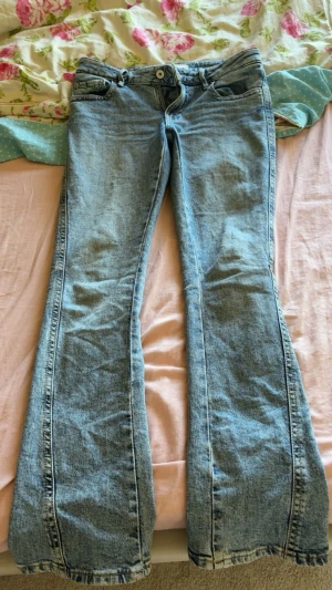 Ljusblå bootcut jeans - Säljer ett par ljusblå bootcut jeans med klassisk femficksdesign och snygga sömmar på bakfickorna. Jeansen har normal midja och är tillverkade i mjukt denimtyg. Perfekta för en avslappnad och trendig look.