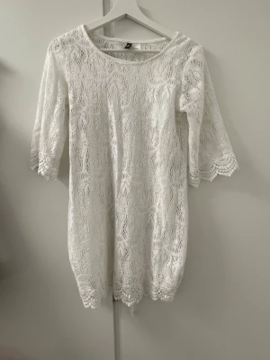 Vit spetsklänning från Divided - Söt vit spetsklänning från Divided by H&M med trekvartsärm och rund halsringning. Klänningen har ett vackert spetsmönster och är fodrad. Perfekt för sommarens alla tillfällen och ger en romantisk vibe.