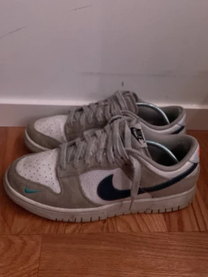 Nike dunk low grå och vit - Nike Dunk Low sneakers i grå mocka, ganska väl använda och smutsiga, samt slit på sulan samt vid hälen, men överlag i ganska bra skick