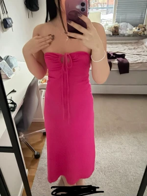 Rosa axelbandslös klänning med snörning - Trendig rosa axelbandslös klänning med snörning framtill och figurnära passform. Klänningen har en enkel, stilren design och är gjord i ett mjukt, stretchigt material som sitter snyggt på kroppen. Perfekt för dig som vill sticka ut med färg.