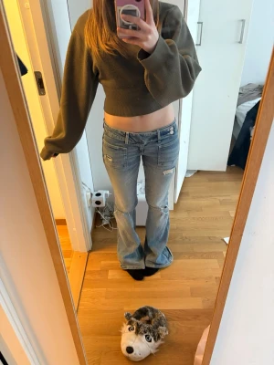 ljusblå jeans från gina - Säljer ett par ljusblå bootcut jeans med slitna detaljer och låg midja. Jeansen har två fickor fram och bak samt slitningar vid knäna och låren för en trendig look. Perfekta för dig som gillar en avslappnad och cool stil.