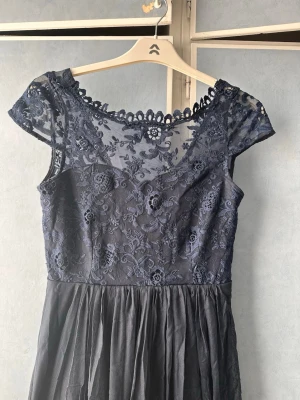 Marinblå klänning med spets VILA - Elegant marinblå långklänning med vacker spets upptill och transparenta detaljer vid axlar och halsringning. Kjolen är i tunt, svepande tyg som ger ett romantiskt intryck. Perfekt för speciella tillfällen där du vill känna dig extra fin.