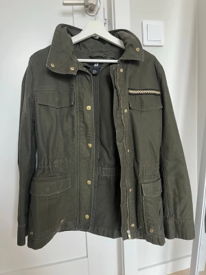 Olivgrön vårjacka från H&M - Vintage och säljs inte mer!! Jättesnygg chic olivgrön/guldig vårjacka. Fina guldiga detaljer och går att styla jätte snyggt. Pris kan diskuteras!!