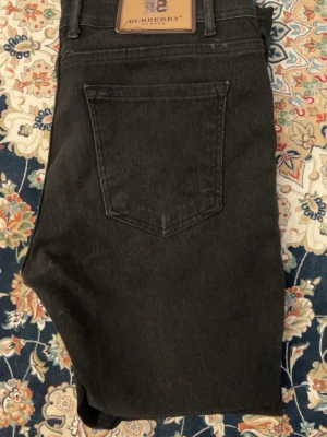 Svarta jeans från Burberry - Snygga svarta jeans från Burberry med klassisk femficksmodell och diskret Burberry-lapp bak i midjan. Jeansen har raka ben och är tillverkade i ett mjukt denimtyg som känns bekvämt och stilrent. Perfekta för dig som vill ha en tidlös och exklusiv look.