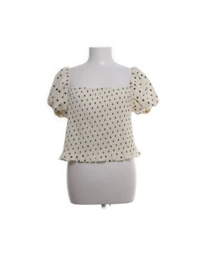 Vit prickig blus med puffärm - Söt vit blus med svarta prickar och puffiga korta ärmar. Toppen har en rak, något croppad passform och volangkant nedtill. Perfekt för dig som gillar en lekfull och trendig stil.