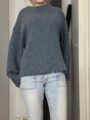 Blågrå stickad tröja - Mysig mörkgrå stickad tröja med avslappnad passform och långa ärmar. Tröjan har en enkel, klassisk design utan synliga detaljer och är perfekt för lager på lager. Passar till jeans eller kjol för en chill look. Den är lite knottrig över hela men är inget man tänker på